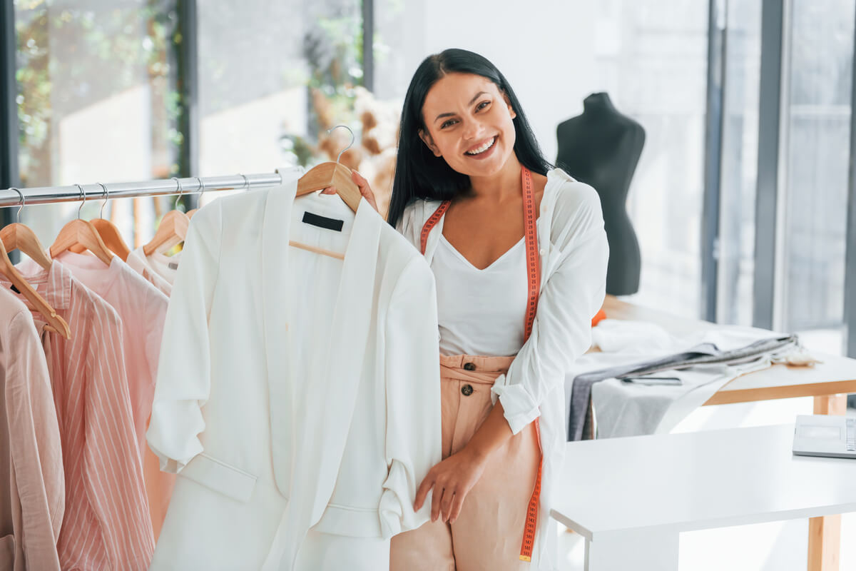 standing-and-smiling-seamstress-is-in-her-office-53ZUC2P Serviços de Uniformes Personalizados | Attelier Visual